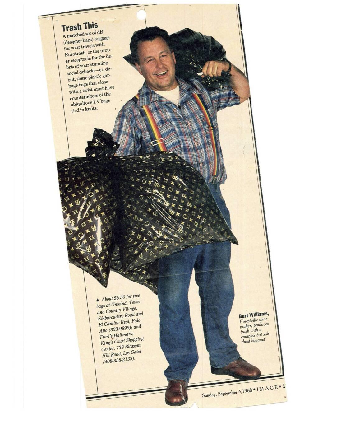 A man in plaid shirt, jeans, and colorful suspenders smiles while holding two black garbage bags with a designer-inspired pattern over his shoulders.