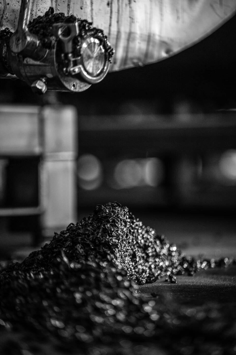 Black and white image of metal shavings piled on the ground below industrial machinery in a workshop setting.